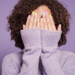 Black woman covering face with pastel nail polish on