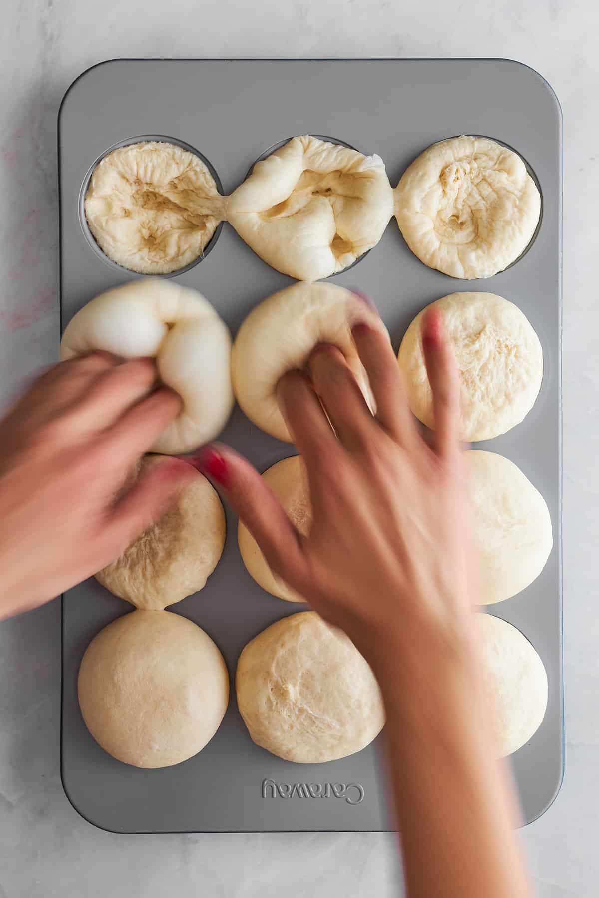 Hände drücken Brötchen in eine Muffinform. 