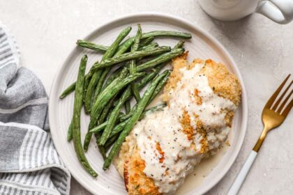 overhead view of chicken cordon bleu covered with sauce on a plate with green beans.