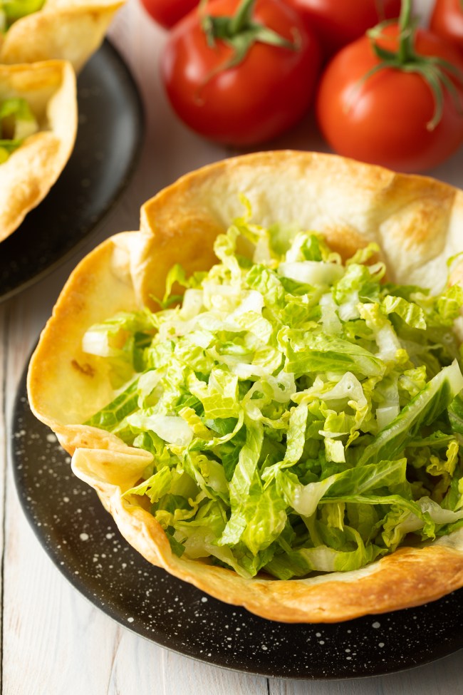Schale einer Taco-Schüssel mit geriebenem Salat darin. 