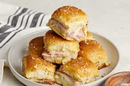 Front side view of a stack of ham and cheese sliders on a plate.