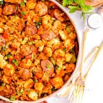 chicken and sausage jambalaya in a skillet next to gold utensils and a red linen towel